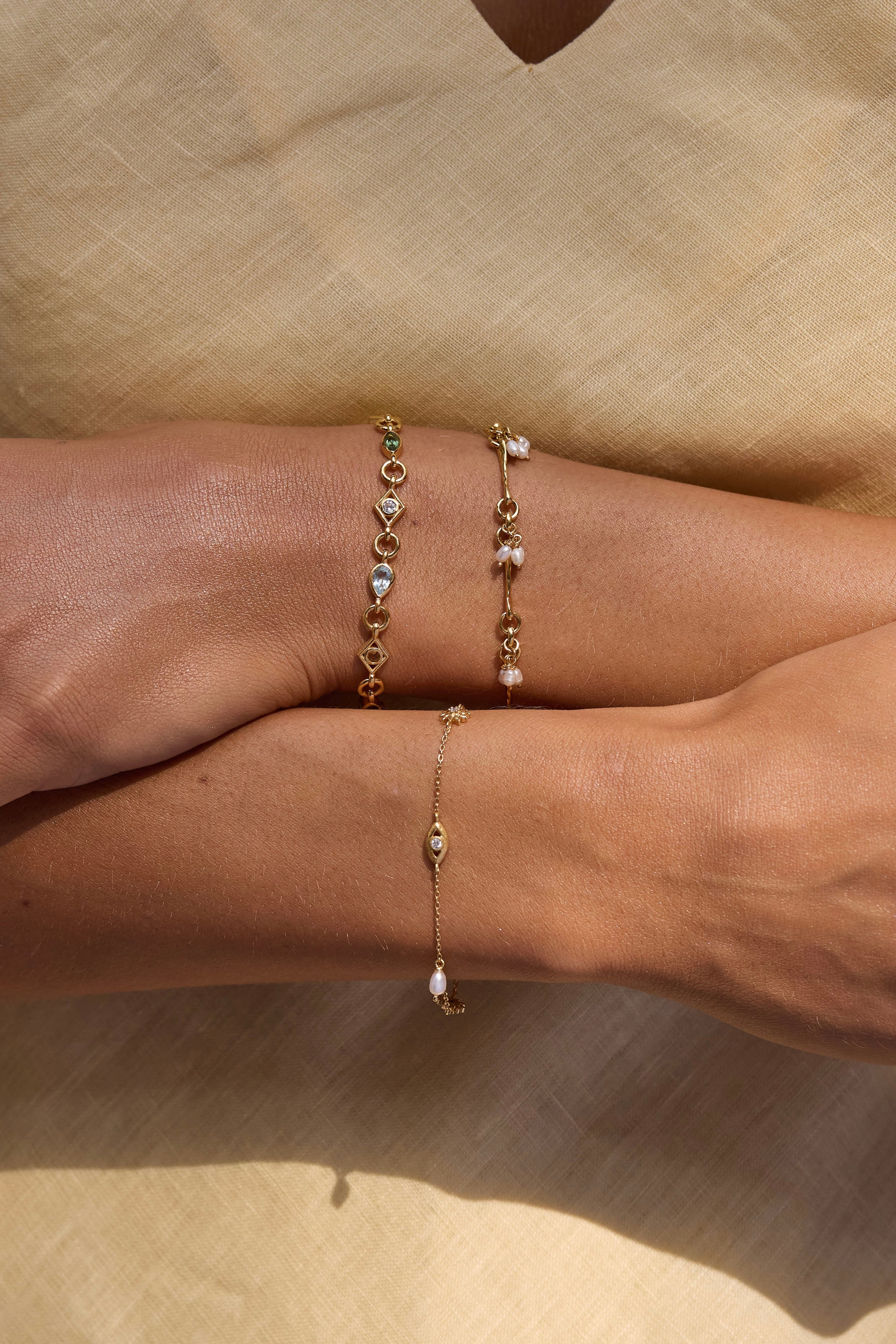 Close-up of a person wearing two gold bracelets with small beads on a beige background